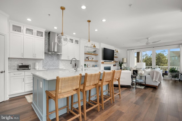 kitchen featuring ceiling fan, wall chimney range hood, light countertops, dark wood-style floors, and white cabinetry