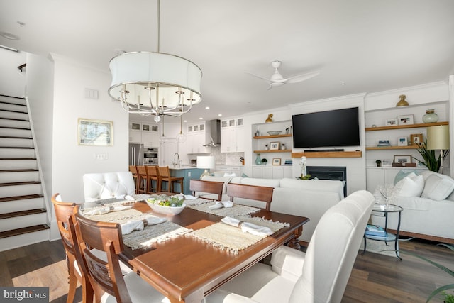 dining room featuring dark wood-type flooring, crown molding, stairs, and ceiling fan with notable chandelier