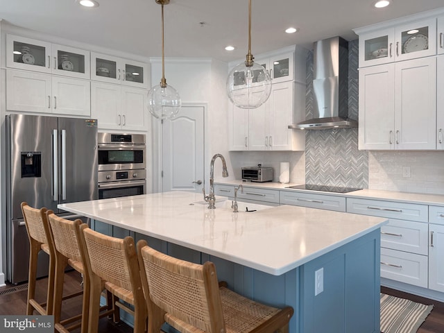 kitchen with stainless steel appliances, wall chimney exhaust hood, light countertops, and a sink