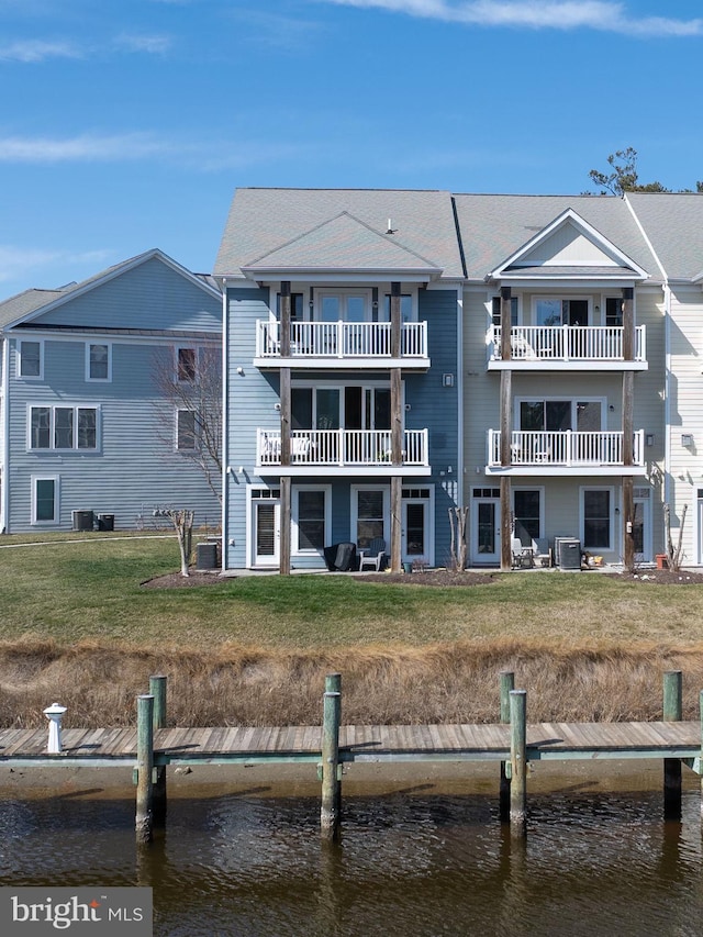 rear view of house with cooling unit, a lawn, and a water view