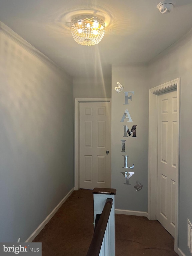 corridor featuring baseboards, dark colored carpet, and a chandelier