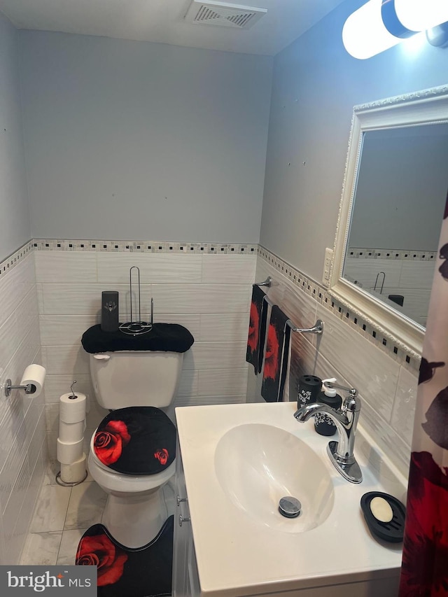 half bath with tile patterned floors, visible vents, toilet, tile walls, and vanity