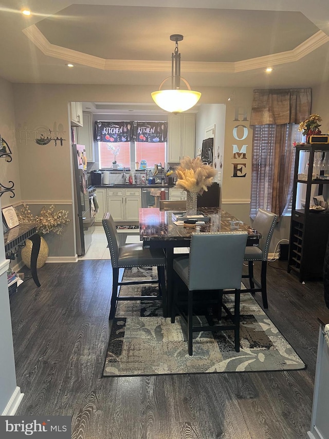 dining space with a raised ceiling, dark wood finished floors, and ornamental molding