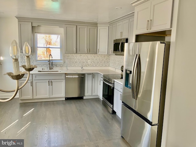 kitchen featuring light countertops, decorative backsplash, light wood-style floors, stainless steel appliances, and a sink