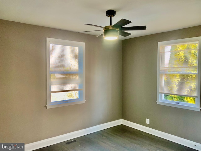 spare room with a ceiling fan, dark wood-style floors, visible vents, and baseboards