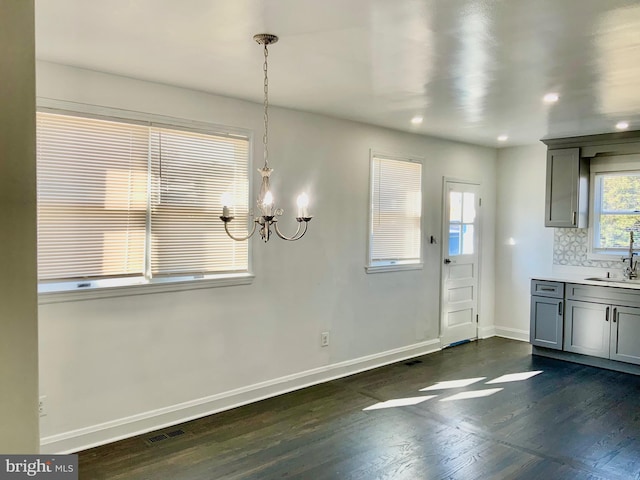 unfurnished dining area featuring visible vents, baseboards, dark wood finished floors, an inviting chandelier, and a sink