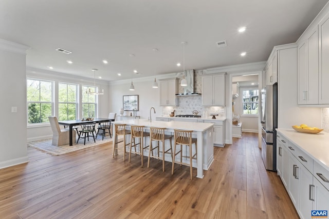 kitchen featuring a kitchen island with sink, visible vents, wall chimney exhaust hood, and light countertops