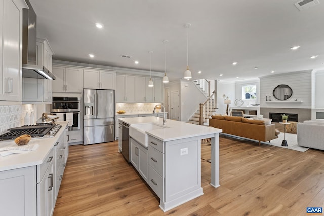 kitchen featuring light wood finished floors, wall chimney range hood, a kitchen bar, appliances with stainless steel finishes, and a sink