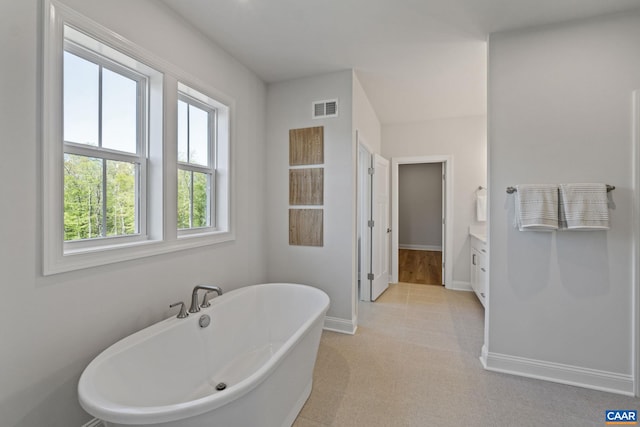 full bath featuring visible vents, baseboards, a freestanding bath, and vanity