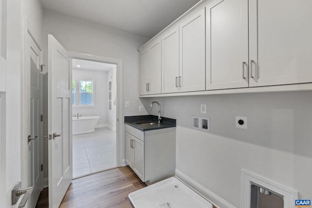 washroom with electric dryer hookup, washer hookup, a sink, cabinet space, and light wood-style floors