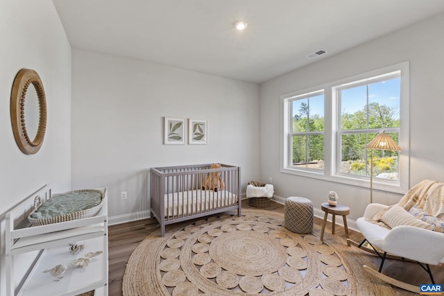 bedroom with visible vents, baseboards, a nursery area, and wood finished floors