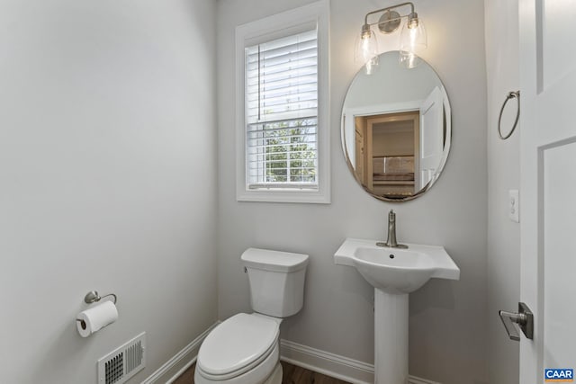 half bath with toilet, baseboards, visible vents, and a sink