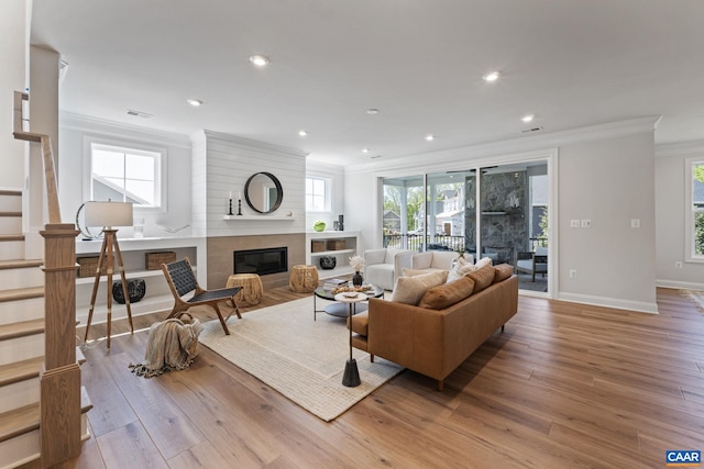 living area featuring wood finished floors, visible vents, stairs, a glass covered fireplace, and crown molding