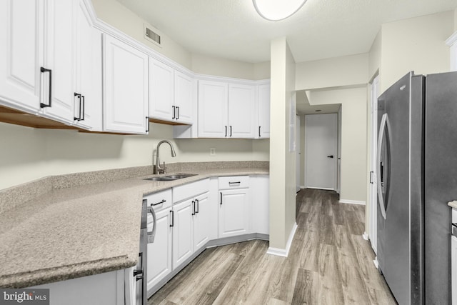 kitchen with visible vents, light wood-style flooring, a sink, white cabinetry, and freestanding refrigerator