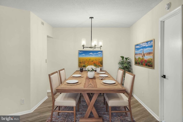 dining area with a notable chandelier, wood finished floors, baseboards, and a textured ceiling