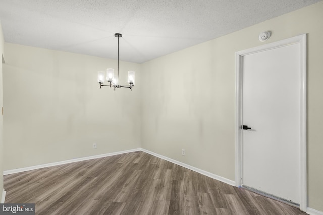 empty room featuring baseboards, wood finished floors, a textured ceiling, and a chandelier