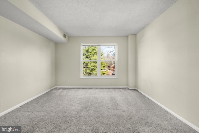 carpeted spare room with visible vents, baseboards, and a textured ceiling