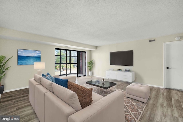 living room featuring visible vents, a textured ceiling, baseboards, and wood finished floors