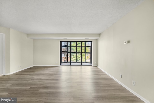 unfurnished room featuring baseboards, a textured ceiling, and wood finished floors