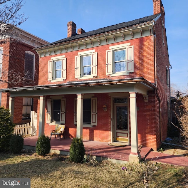 rear view of property featuring brick siding, covered porch, and a chimney