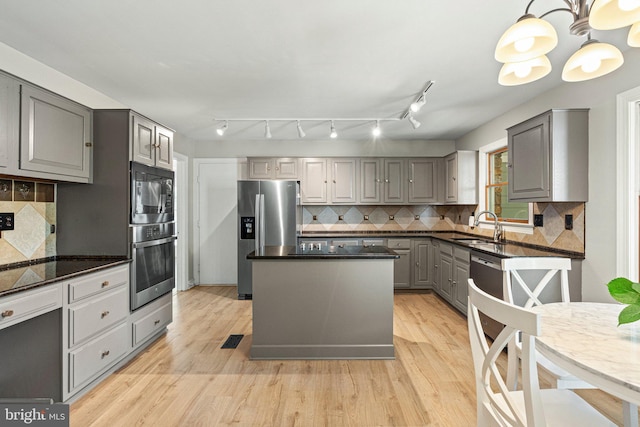 kitchen featuring a kitchen island, a sink, gray cabinetry, light wood-style floors, and appliances with stainless steel finishes