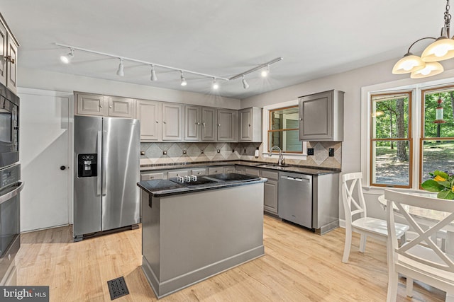 kitchen featuring gray cabinetry, a sink, backsplash, light wood-style floors, and appliances with stainless steel finishes