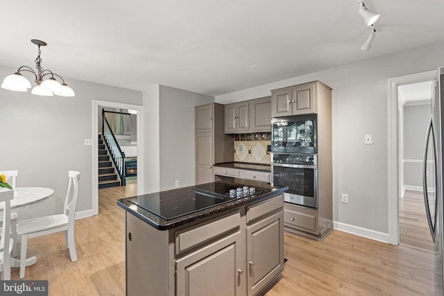 kitchen featuring light wood finished floors, backsplash, gray cabinets, an inviting chandelier, and stainless steel appliances