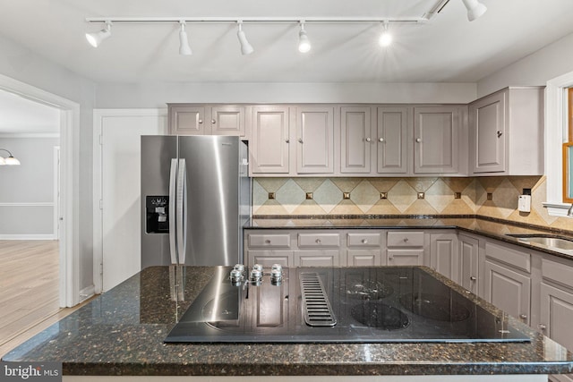 kitchen with black electric stovetop, stainless steel fridge, backsplash, and a sink