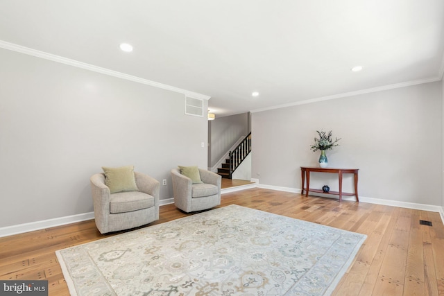 living area featuring hardwood / wood-style flooring, crown molding, visible vents, and baseboards