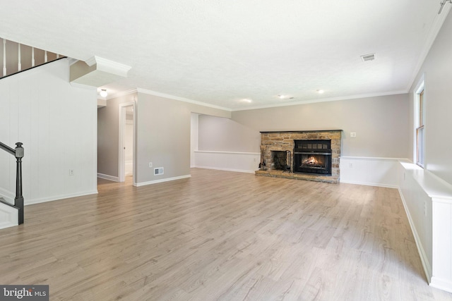 unfurnished living room with baseboards, visible vents, light wood-style flooring, ornamental molding, and a stone fireplace