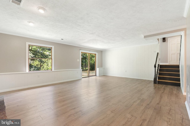 unfurnished living room featuring visible vents, a textured ceiling, wood finished floors, crown molding, and stairs