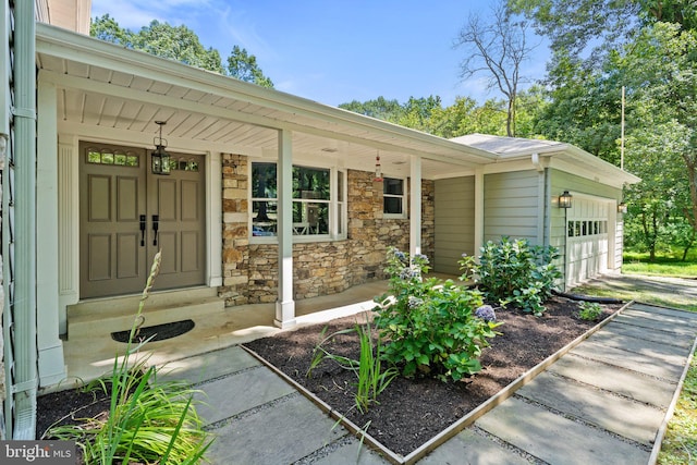 doorway to property featuring stone siding, a porch, and an attached garage