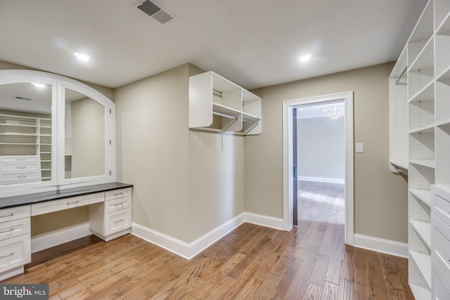 walk in closet with visible vents, built in study area, and light wood-type flooring