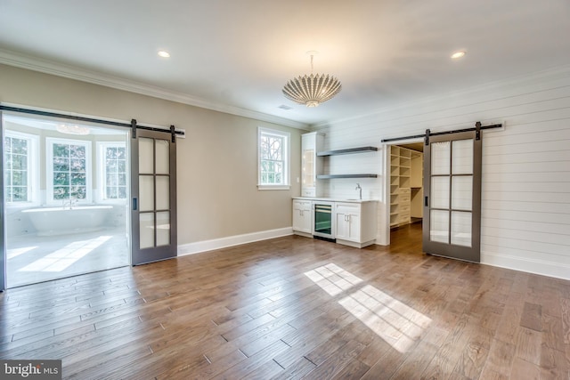 unfurnished living room featuring a barn door, wine cooler, dark wood-type flooring, and crown molding