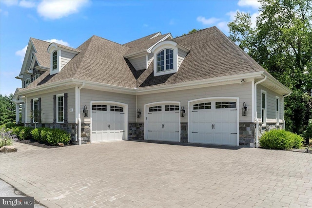 view of side of home featuring a garage, stone siding, driveway, and a shingled roof