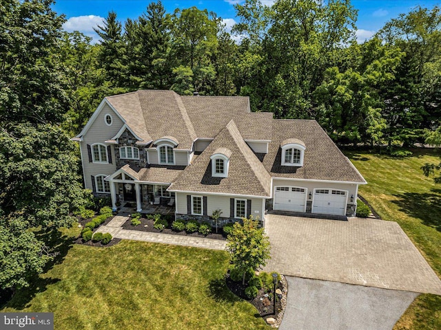 view of front of property featuring covered porch, concrete driveway, a front yard, and a shingled roof