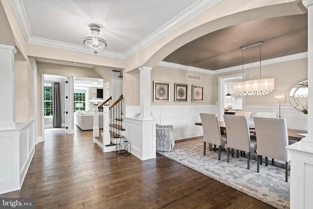 dining area with visible vents, dark wood-style floors, crown molding, a decorative wall, and decorative columns