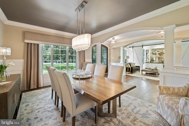 dining room with a barn door, crown molding, wood finished floors, and arched walkways