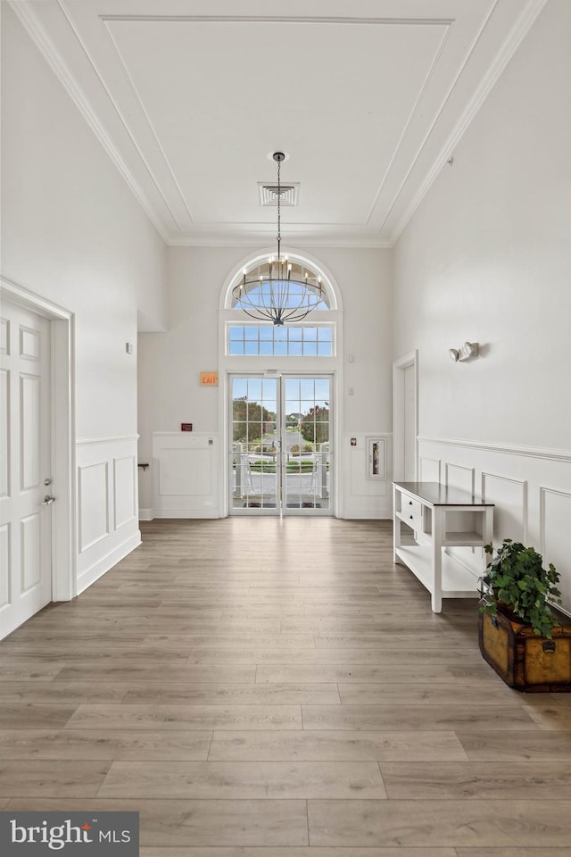 entrance foyer with visible vents, light wood-style floors, crown molding, a decorative wall, and a chandelier