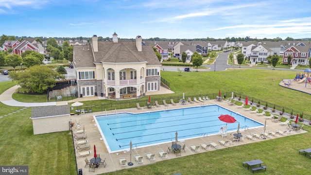 community pool featuring a patio, fence, a lawn, and a residential view