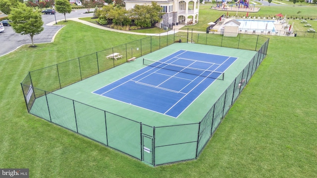 view of tennis court with a yard and fence