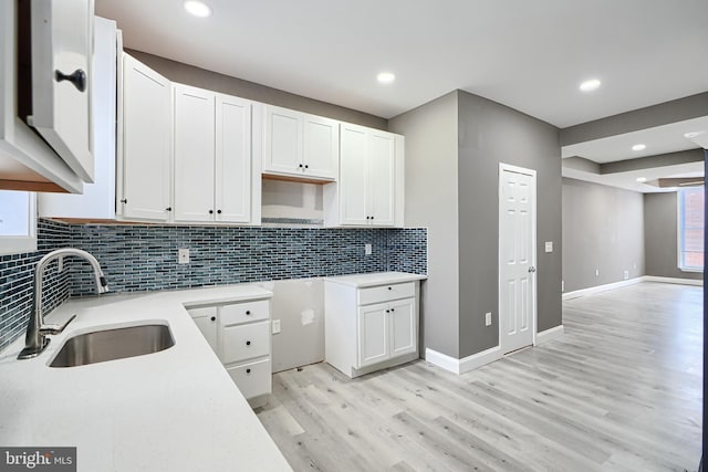 kitchen featuring baseboards, a sink, light wood-style floors, white cabinetry, and backsplash