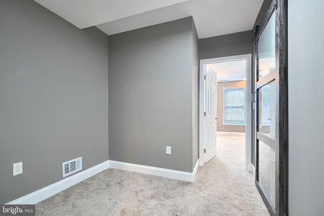 empty room featuring visible vents, carpet floors, baseboards, and a barn door