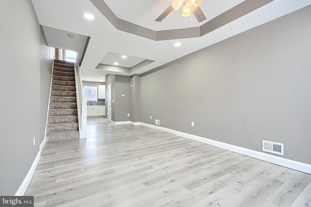 unfurnished living room with visible vents, baseboards, light wood finished floors, ceiling fan, and a raised ceiling