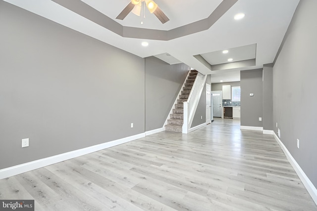 interior space with a tray ceiling, stairway, a ceiling fan, and light wood-type flooring