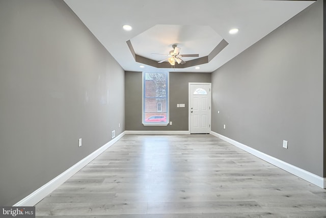 entryway featuring light wood-type flooring, baseboards, a raised ceiling, and a ceiling fan