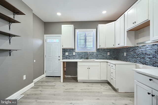 kitchen featuring a sink, light countertops, decorative backsplash, light wood-style floors, and open shelves