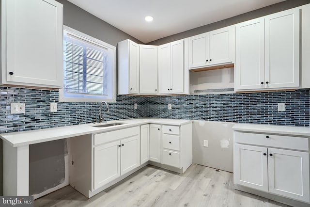 kitchen featuring a sink, decorative backsplash, light wood-style flooring, and white cabinets