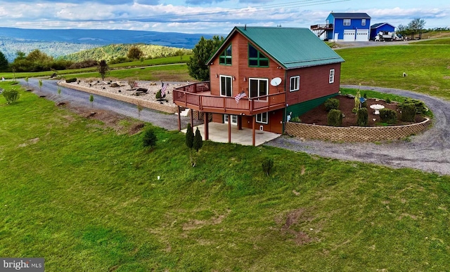 view of side of property featuring a lawn, a deck with mountain view, driveway, a patio, and metal roof