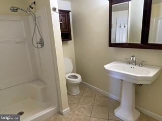 bathroom featuring toilet, a stall shower, a sink, tile patterned flooring, and baseboards